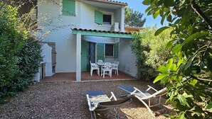 Une maison dotée d’un patio comprenant une table et des chaises, entouré de gravier et de verdure.