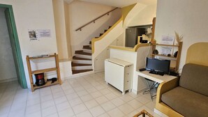 Un espace de vie compact comprenant un escalier, une petite kitchenette, un canapé et un bureau avec un ordinateur.