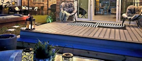 Um pátio externo com deck de madeira, duas cadeiras suspensas e uma mesa com lanternas decorativas.