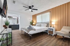 Ein Schlafzimmer mit Bett, Nachttisch, Lampe und Blick auf die Küche.
