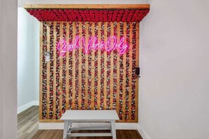 Ein Zimmer mit einer holzverkleideten Wand, verziert mit vertikalen floralen Mustern, und einem Neon-Schild mit der Aufschrift 'Good Vibes Only'.