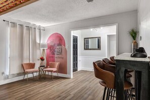 Ett modernt vardagsrum med trägolv, en rosa vägg med en väggmålning som föreställer en stadsbild, en matplats med bord och stolar samt en stor spegel.