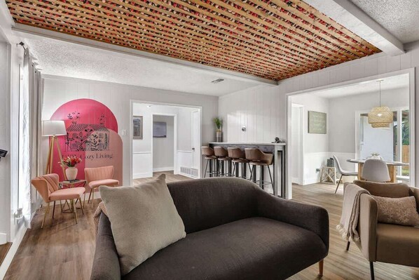 A modern living room with a dark sofa, a pink accent wall, and a ceiling with a patterned design.