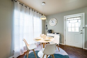A dining area with a round table, white chairs, a clock, and a window with curtains.