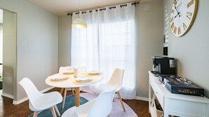 Un coin repas avec une table ronde, des chaises blanches, une machine à café et un jeu de poker posé sur une petite table d’appoint.