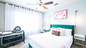 Une chambre à coucher comprenant un lit, un bureau, une poussette, un ventilateur de plafond et une lampe fixée au mur.