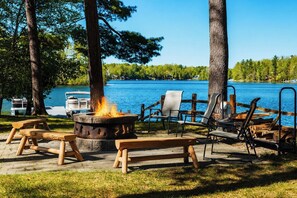 Un espace extérieur aménagé au bord du lac, avec un foyer, des bancs et des fauteuils de détente.
