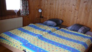 A wooden-paneled room with a double bed, a bedside lamp, and a window with floral curtains. - Outside: Chalet of about 132m2, for 10 people, with garden and garden furniture -Inside: living room (Chandolin)