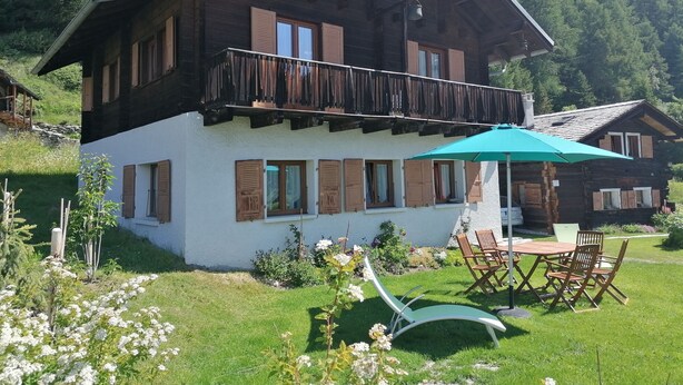 A two-story chalet with a balcony, a patio with a table and chairs, and a garden with flowers. - Outside: Chalet of about 132m2, for 10 people, with garden and garden furniture -Inside: living room (Chandolin)