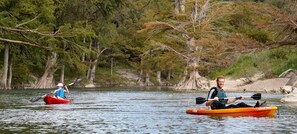 Two people kayaking on a calm river surrounded by trees.