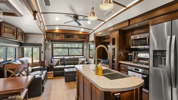 A spacious RV kitchen with a central island, stainless steel appliances, and a seating area with a sofa and table.