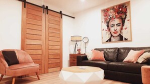 Una sala de estar moderna con un sofá de cuero negro, un sillón rosa, suelo de madera y un cuadro grande en la pared.