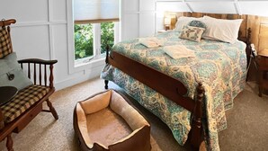 Une chambre à coucher avec un grand lit, une chaise en bois, une petite table et une fenêtre donnant sur un paysage verdoyant.