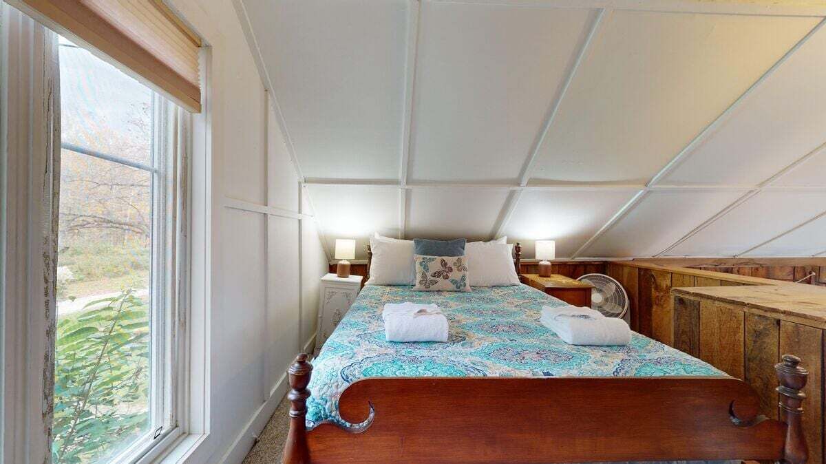 A bedroom with a large window, a wooden bed, and a ceiling with exposed beams.