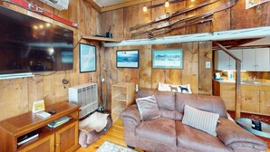 Un intérieur de chalet chaleureux avec un grand téléviseur à écran plat, des murs en bois, un canapé et un coin cuisine.