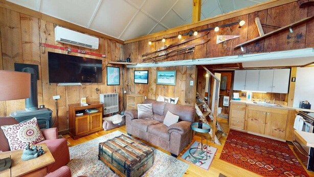 Une chambre confortable, aménagée dans le style d’un chalet, avec un canapé, une table à manger en bois, un coin cuisine et une mezzanine équipée d’un téléviseur.