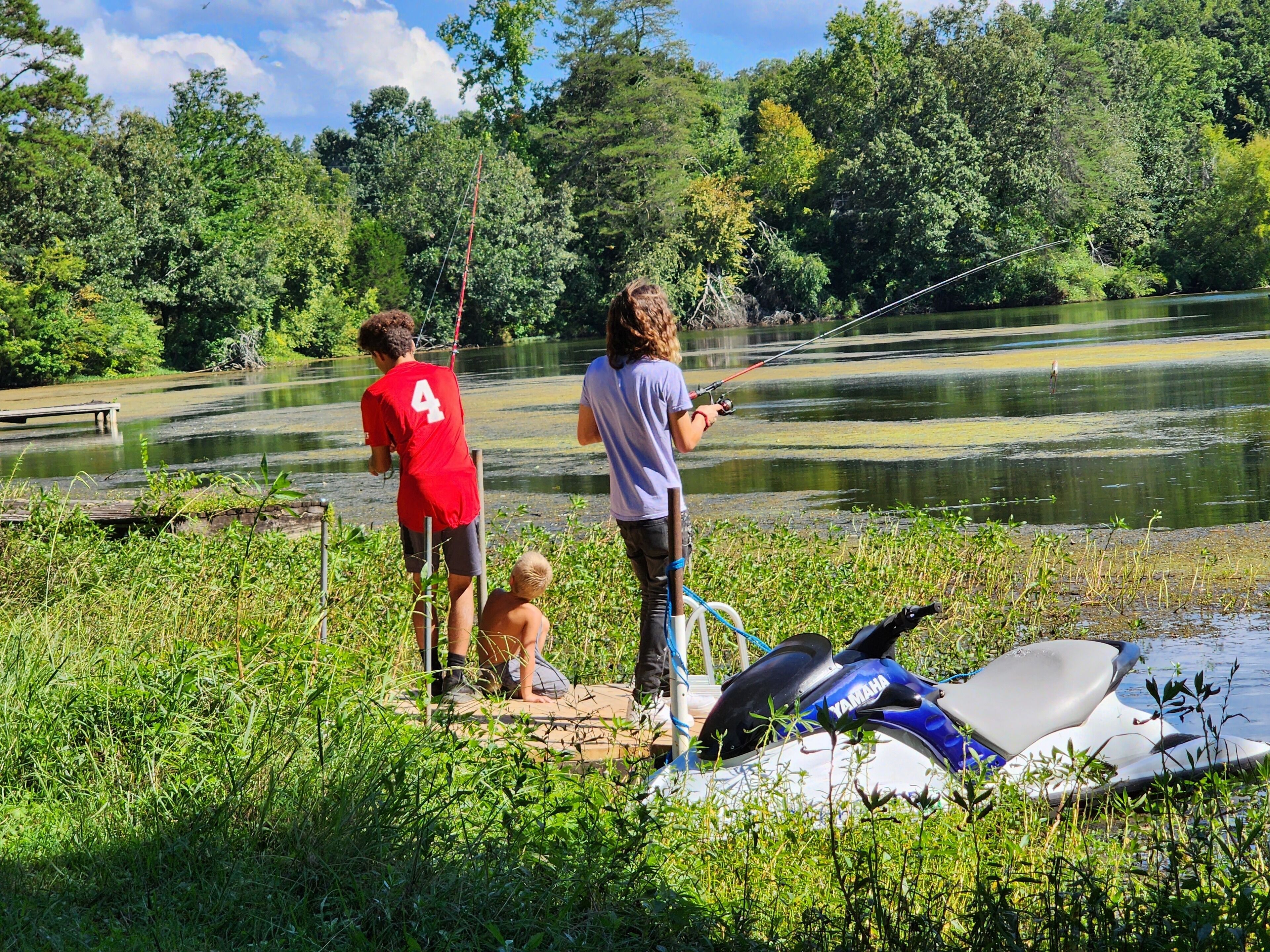 A lakeside scene with people fishing and a Yamaha jet ski in the foreground.