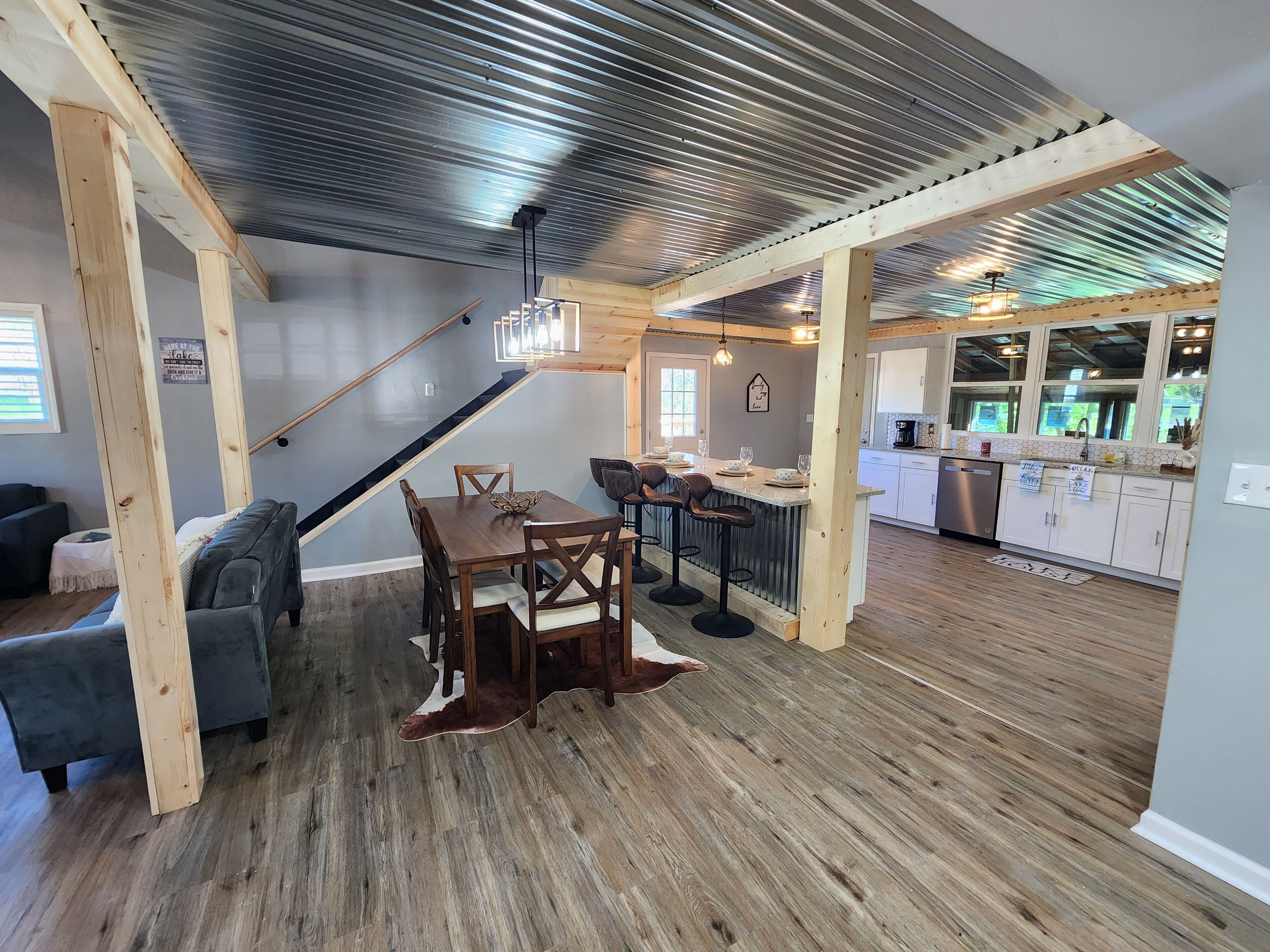 Un vaste espace de salle à manger avec une table et des chaises en bois, une cuisine dotée de meubles blancs et un escalier menant à un autre niveau.