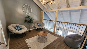 Une pièce confortable de style loft, avec un haut plafond, un lustre, une grande fenêtre et un balcon.