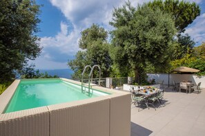 A swimming pool with a view, surrounded by greenery and a table with chairs.