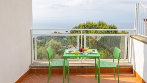 Ein Balkon mit Frühstückstisch, Stühlen und Blick auf das Meer und Grünflächen.