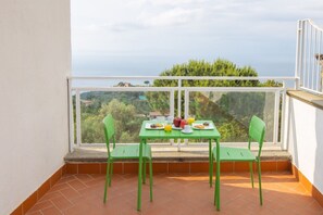 Un balcón con una mesa dispuesta para el desayuno, sillas y vistas al mar y la vegetación.