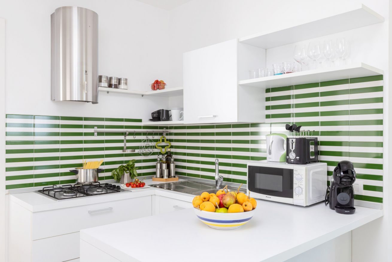 A modern kitchen with a gas stove, a microwave, a coffee maker, and a bowl of fruit on the counter.