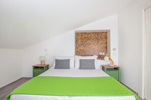 Un lit simple avec une couverture verte, deux tables de chevet avec des lampes et un mur décoré au-dessus du lit.