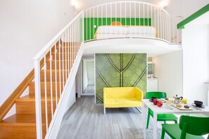Un espace de vie de style loft avec un escalier, un canapé jaune, une table à manger où le petit-déjeuner est servi, et un mur d’accent vert.