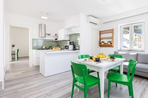 A modern kitchen with a central island, white cabinetry, and green chairs at a dining table.