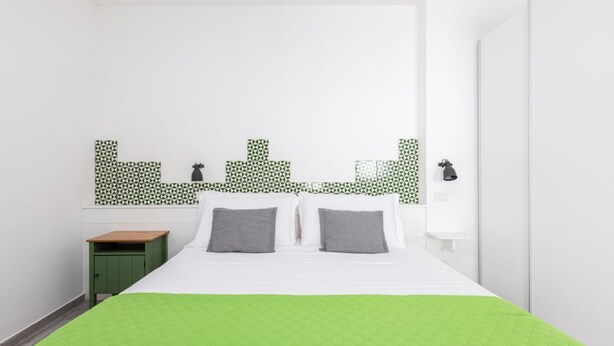 Ein Schlafzimmer mit einem Bett, Kissen, einem Nachttisch, einem grünen Schrank und einer Wand mit geometrischem Muster.