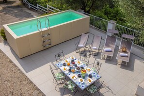 Une piscine équipée d’un escalier, de chaises longues et d’une table où sont servis des plats et des boissons.