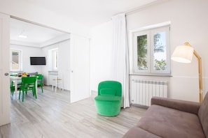 Una habitación moderna con zona de comedor, una silla verde, un sofá marrón y una ventana con cortinas.
