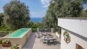 A rooftop pool with a view of the sea, a dining area with outdoor furniture, and a statue on the building.