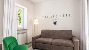 Ein Zimmer mit einem braunen Sofa, einem grünen Sessel, einem Fenster mit weißen Vorhängen und einer Wand mit motivierendem Text.