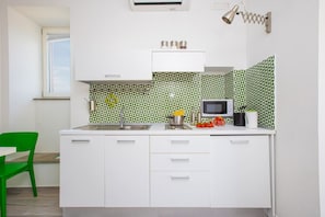 Une cuisine avec des meubles blancs, un four à micro-ondes et une fenêtre.