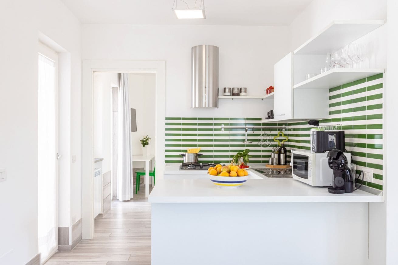 Een moderne keuken met een wit aanrecht, een groene streepjesachtergrond en een roestvrijstalen afzuigkap.