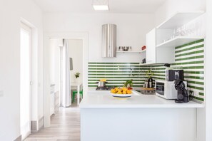 Una cocina moderna con encimera blanca, salpicadero verde a rayas y campana extractora de acero inoxidable.