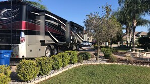 A large tour bus parked in a residential area with a well-maintained lawn and a stone pathway. - Motorhome Pad - Mt. Olive Shores North (Polk City)