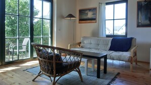 A spacious living room with a large window, a sofa, a wicker chair, and a table.