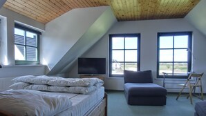 A bedroom with a sloped ceiling, a bed, a television, and large windows.