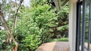 A wooden deck with a view of dense greenery and a building with large windows.