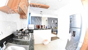 A modern kitchen with a gas stove, a refrigerator, and a dining area with a sofa and artwork. - Apartamento EN LAS Carreras Centro DE LA Ciudad (Santiago)