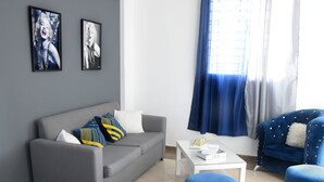 A modern living room with a grey sofa, blue ottomans, a white coffee table, and two framed pictures on the wall. - Apartamento EN LAS Carreras Centro DE LA Ciudad (Santiago)