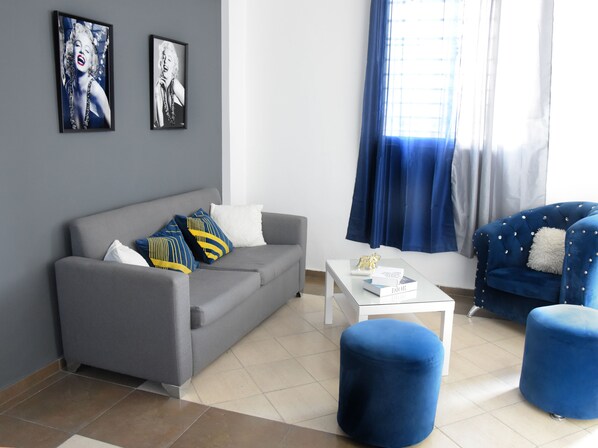 A modern living room with a grey sofa, blue ottomans, a white coffee table, and two framed pictures on the wall.