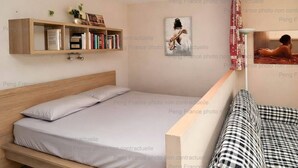 Un dormitorio con cama, mesita de noche, estantería, un cuadro y una ventana con cortinas.