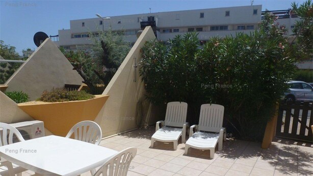 Un patio al aire libre con mesa y sillas, una maceta grande y una fila de sillones reclinables.