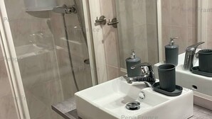 Une salle de bain avec une douche à parois de verre, un lavabo blanc doté d’un robinet moderne et un miroir au-dessus du lavabo.