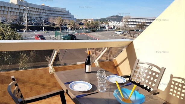 Un balcon avec une table dressée pour deux personnes, une bouteille de vin et un saladier bleu contenant des couverts.