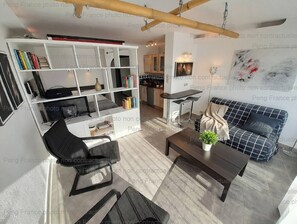 Een moderne woonkamer met een zwarte bank, een witte boekenkast en een eethoek met een barkruk.